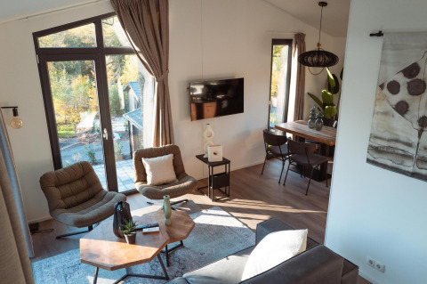 Intérieur de lodge lumineux et moderne avec grandes fenêtres, fauteuils confortables et table en bois.