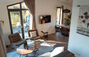 Bright, modern lodge interior with large windows, cozy chairs, wooden table, TV and inviting decor.