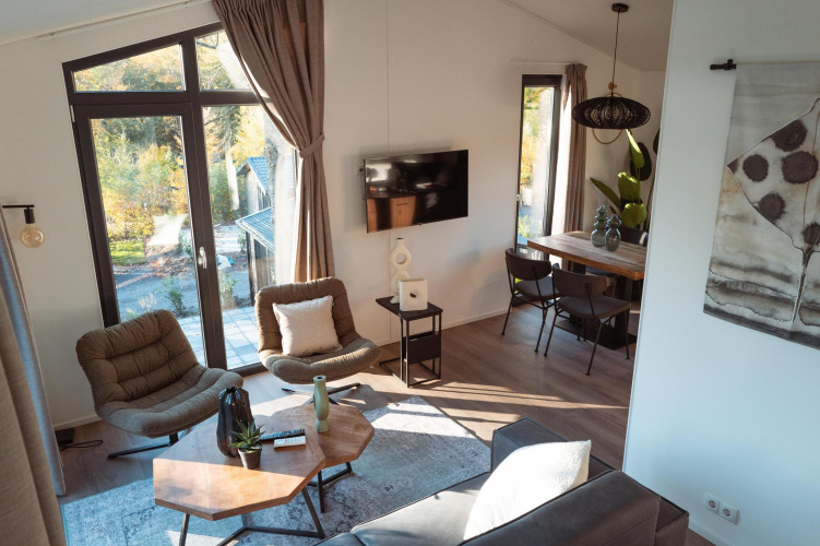 Bright, modern lodge interior with large windows, cozy chairs, wooden table, TV and inviting decor.