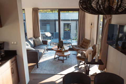 Salon moderne et chaleureux d’un lodge avec grandes baies vitrées, fauteuils confortables et terrasse extérieure.
