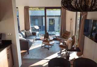 Salon moderne et chaleureux d’un lodge avec grandes baies vitrées, fauteuils confortables et terrasse extérieure.