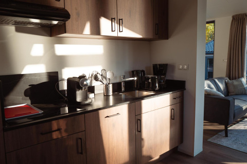Kitchenette moderne de lodge avec plans de travail noirs, meubles en bois et ustensiles baignant au soleil.