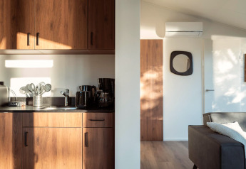 Solrigt interiørbillede af et moderne lodgekøkken med træskabe, apparater og en hyggelig stue.