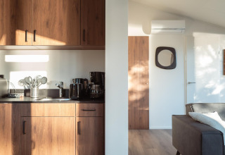 Zonnig interieur van een moderne lodge met houten keukenkasten, apparaten en een gezellige zithoek.