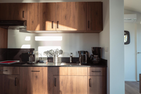 Cocina moderna en un lodge con gabinetes de madera, cafetera, hervidor y utensilios en luz matutina.