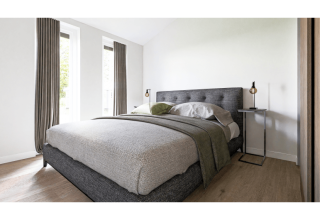 Chambre moderne de lodge avec literie grise, grandes fenêtres, rideaux et mobilier contemporain élégant.