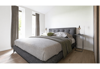 Chambre moderne de lodge avec literie grise, grandes fenêtres, rideaux et mobilier contemporain élégant.