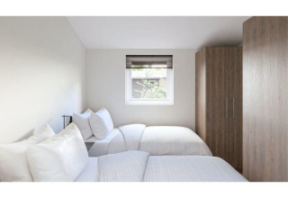 Habitación luminosa y moderna en un lodge con dos camas individuales, ventana y grandes armarios de madera.