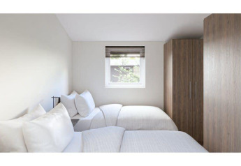Chambre lumineuse et moderne dans un lodge avec deux lits simples, fenêtre et grandes armoires en bois.