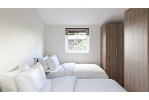 Habitación luminosa y moderna en un lodge con dos camas individuales, ventana y grandes armarios de madera.