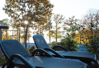 Deux chaises longues sur une terrasse donnant sur des arbres et un lac, soleil filtrant à travers.