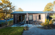 Modern lodge with patio, lounge chairs, dining set and umbrella, surrounded by trees in autumn.