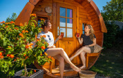 Dos mujeres disfrutan de bebidas frente a una cabaña de madera llamada Tractor cabin en Biggesee, Alemania.