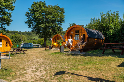 Zwei Personen entspannen vor Traktorkabinen-Lodges am Biggesee in Deutschland an einem sonnigen Tag.