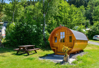 Cabaña tractor en Biggesee, Alemania. Lodge de madera en forma de barril y mesa de picnic en entorno verde.