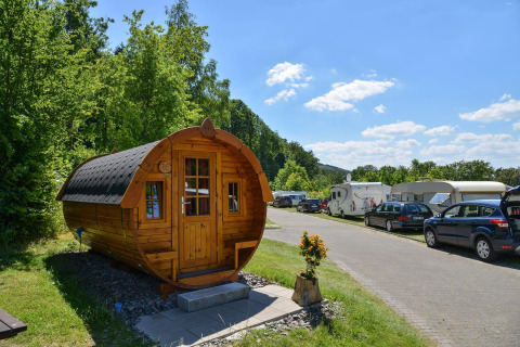 Traktorkabine am Biggesee in Deutschland, umgeben von Wohnwagen, Autos und grüner Natur bei Sonnenschein.