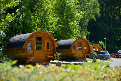 Cabañas de tractor en Biggesee, Alemania, rodeadas de vegetación y coches aparcados cerca.