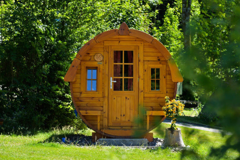 Cabaña redonda de madera llamada Tractor Cabin en Biggesee, Alemania, rodeada de vegetación y flores.
