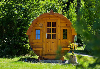 Cabaña redonda de madera llamada Tractor Cabin en Biggesee, Alemania, rodeada de vegetación y flores.