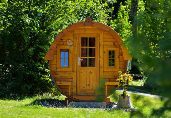 Et rundt træhus kaldet Tractor Cabin ved Biggesee i Tyskland, omgivet af frodigt grønt og blomster.