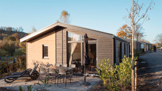 Outdoor view of the Hackfort MIVA lodge with a patio, dining set, loungers, and clear blue sky.