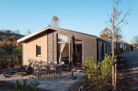 Vue extérieure du lodge Hackfort MIVA avec terrasse, mobilier de jardin et transats sous ciel bleu.