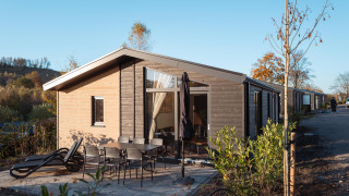 Vue extérieure du lodge Hackfort MIVA avec terrasse, mobilier de jardin et transats sous ciel bleu.