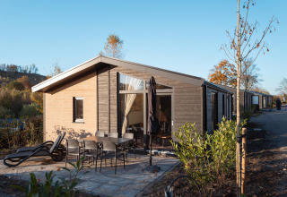 Vue extérieure du lodge Hackfort MIVA avec terrasse, mobilier de jardin et transats sous ciel bleu.