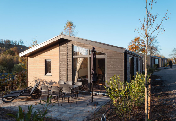 Vue extérieure du lodge Hackfort MIVA avec terrasse, mobilier de jardin et transats sous ciel bleu.