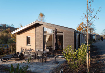 Vue extérieure du lodge Hackfort MIVA avec terrasse, mobilier de jardin et transats sous ciel bleu.