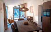 Modern lodge Hackfort MIVA at Biggesee, Germany, featuring dining table, cozy sofa, and large windows.