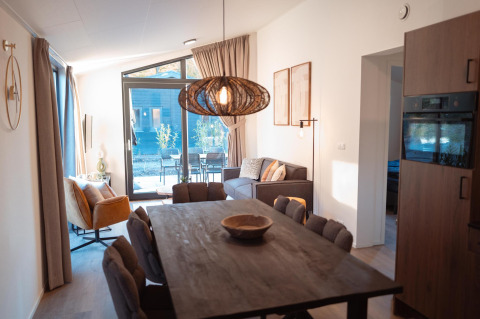 Modern lodge Hackfort MIVA at Biggesee, Germany, featuring dining table, cozy sofa, and large windows.