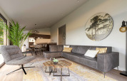 Modern lodge living room with gray sofa, large plant, round wall art, and open kitchen in the background.