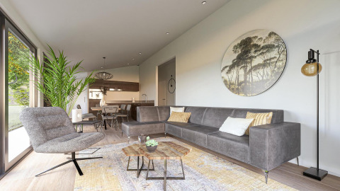 Moderne lodge woonkamer met grijze zetel, grote plant, ronde wanddecoratie en open keuken achteraan.