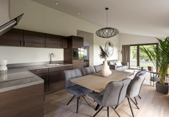 Moderne lodge met open keuken, eetruimte, gezellige zithoek en grote ramen met zicht op het groen.