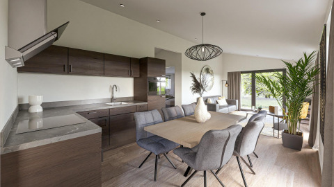 Intérieur de lodge moderne avec cuisine ouverte, salle à manger, salon lumineux et grandes fenêtres sur la verdure.