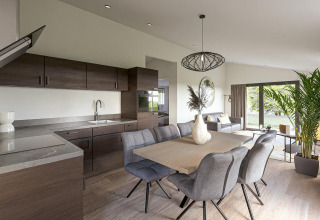 Intérieur de lodge moderne avec cuisine ouverte, salle à manger, salon lumineux et grandes fenêtres sur la verdure.