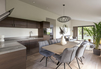 Moderne lodge med åbent køkken, spisebord og stue, store vinduer og grønne planter i lys atmosfære.