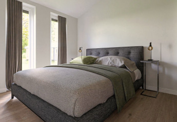 Dormitorio moderno en una cabaña con grandes ventanas, cama gris, diseño minimalista y pisos de madera.