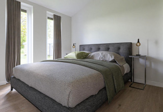 Dormitorio moderno en una cabaña con grandes ventanas, cama gris, diseño minimalista y pisos de madera.