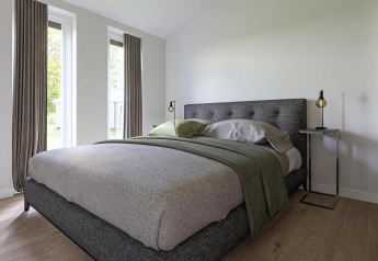 Chambre moderne dans un lodge avec grandes fenêtres, lit gris, décoration minimaliste et tables de nuit.