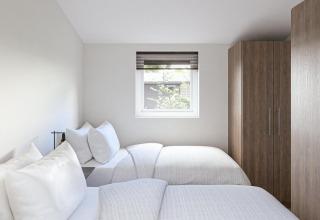 Habitación luminosa en una cabaña con dos camas individuales, ropa de cama blanca, ventana y armario.