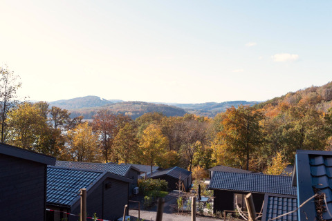 View from a lodge with black roofs overlooking colorful autumn trees and hills under a clear sky.
