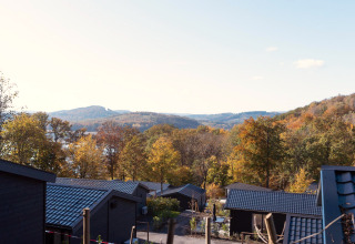 View from a lodge with black roofs overlooking colorful autumn trees and hills under a clear sky.