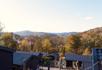 Uitzicht vanaf een lodge met zwarte daken op herfstbomen en heuvels onder een heldere lucht.