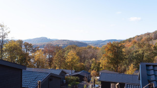 Vista da un lodge con tetti neri su alberi autunnali colorati e colline sotto un cielo limpido.