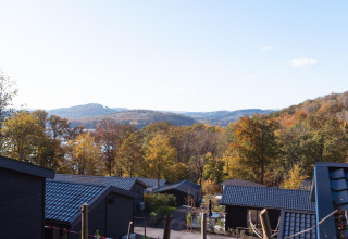 Blick von einer Lodge mit schwarzem Dach auf herbstliche Bäume und Hügel unter blauem Himmel.