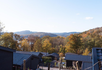 Blick von einer Lodge mit schwarzem Dach auf herbstliche Bäume und Hügel unter blauem Himmel.