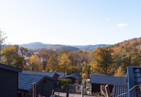 Vue depuis un lodge au toit noir sur des arbres d'automne colorés et des collines sous un ciel bleu.