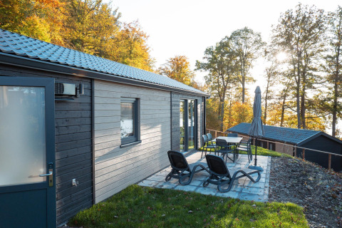 Terrasse extérieure avec chaises longues et table à la lodge Hackfort, au cœur de la forêt automnale.